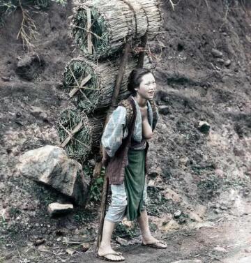 a very cheerful japanese woman carrying three huge tawara (rice straw bags) filled with charcoal on what appears to be a lonely country road. c.1890.