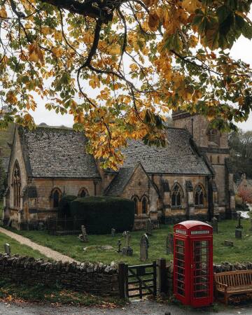 bright red telephone box next to the st barnabas church in snowshill, a small cotswolds village in gloucestershire, england.