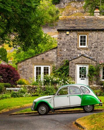 citroën 2cv in front of a stone cottage in kettlewell, a small village in upper wharfedale, north yorkshire, england.